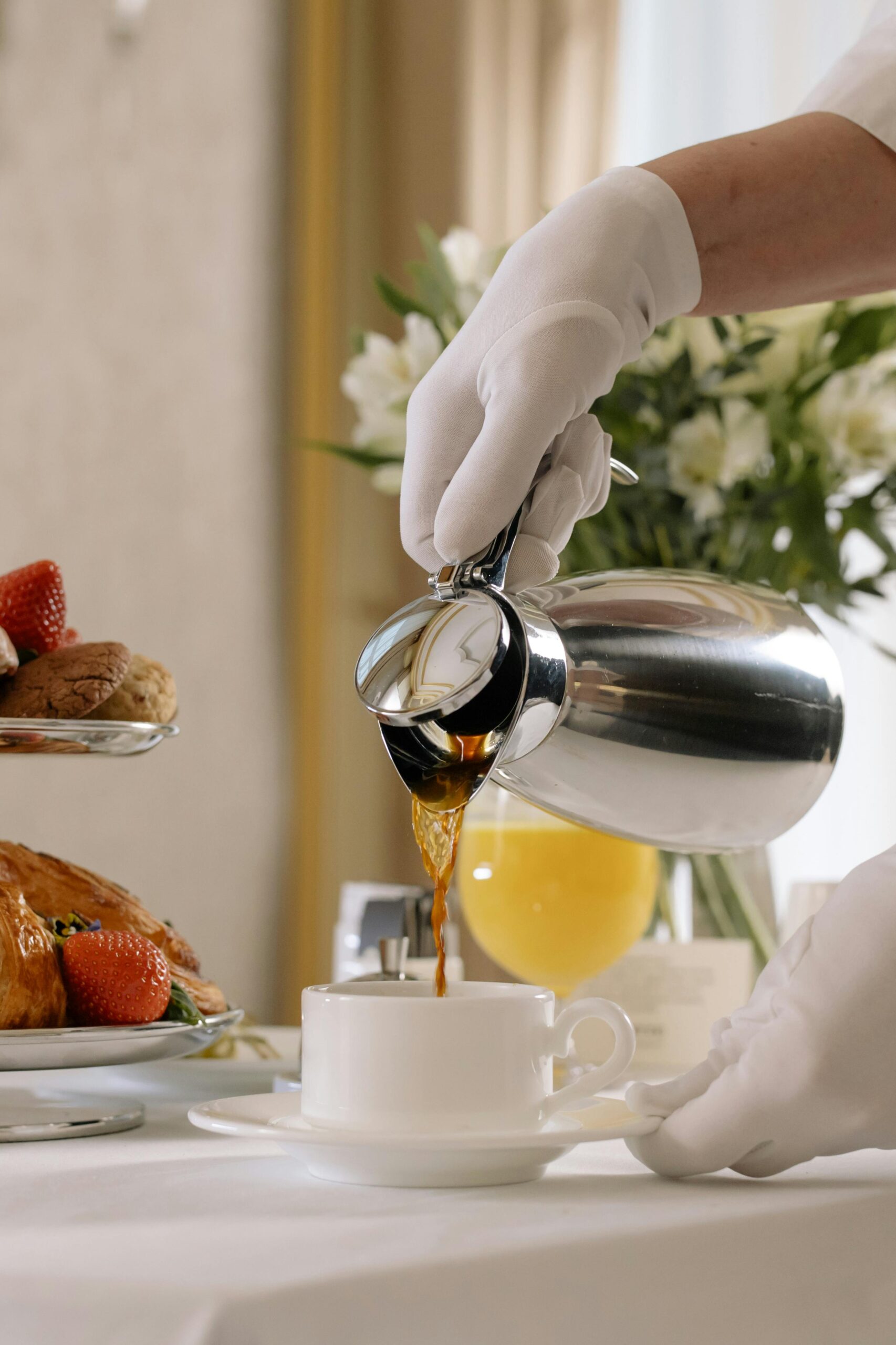 Elegant morning setup with coffee and pastries served by a gloved hand, showcasing luxury room service.